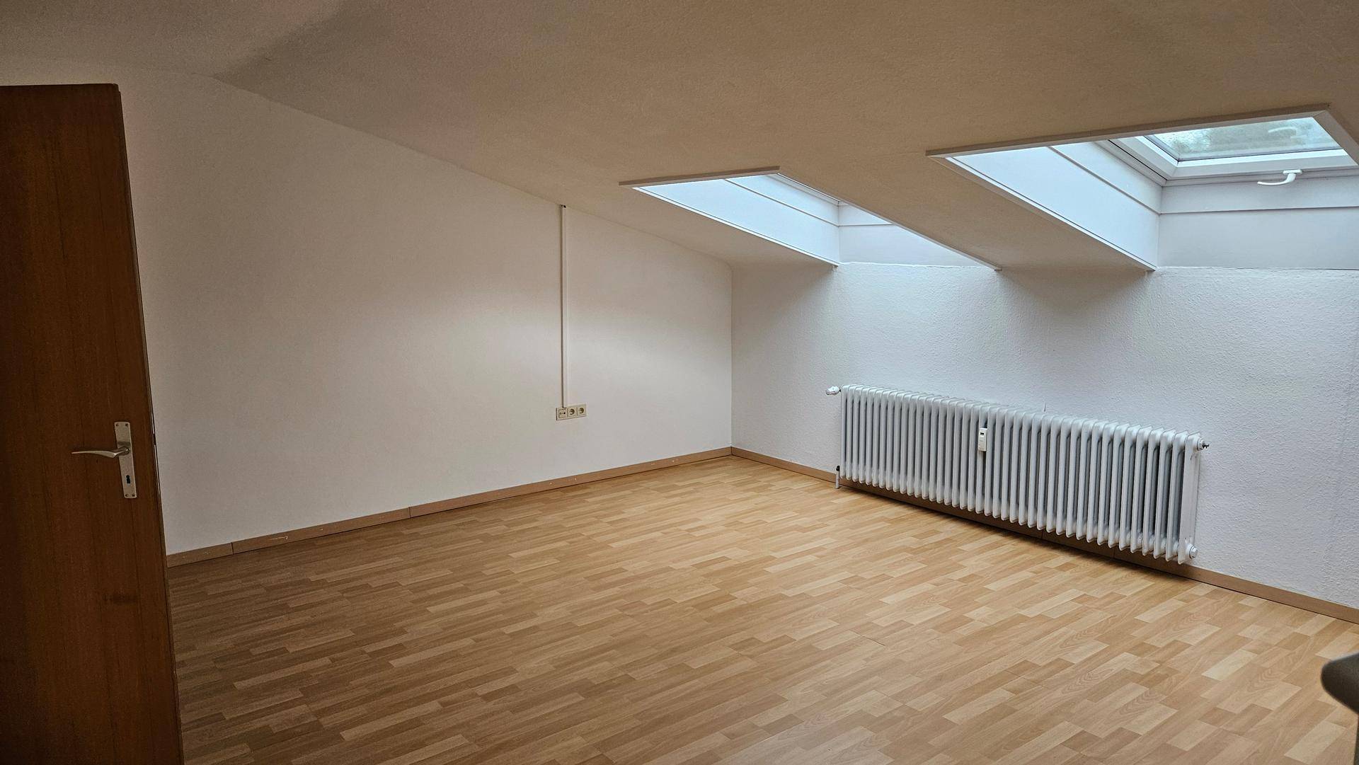 Heller Raum im Dachgeschoss mit Laminatboden, Dachschräge und zwei Dachfenstern.
