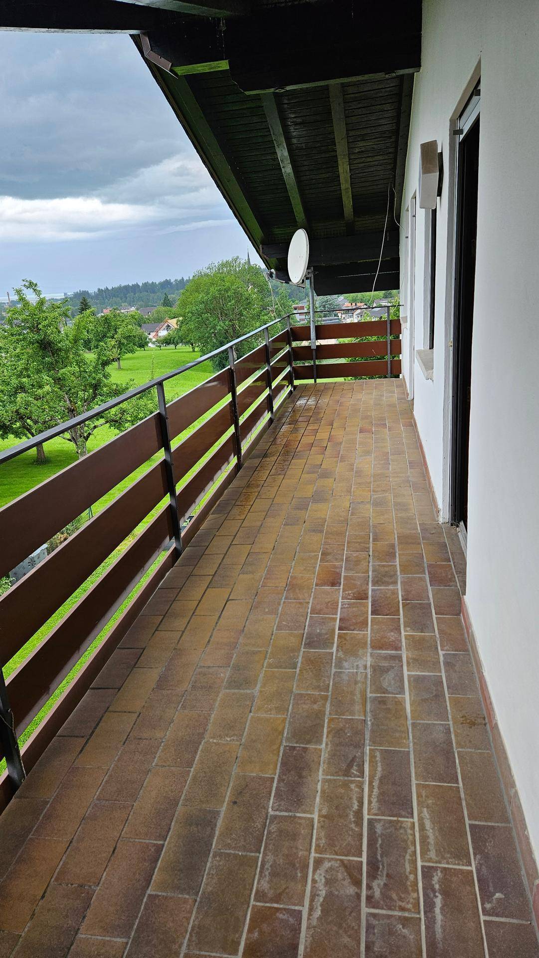 Langer Balkon mit Terrakottafliesen, Holzgeländer und weitem Blick ins Grüne.