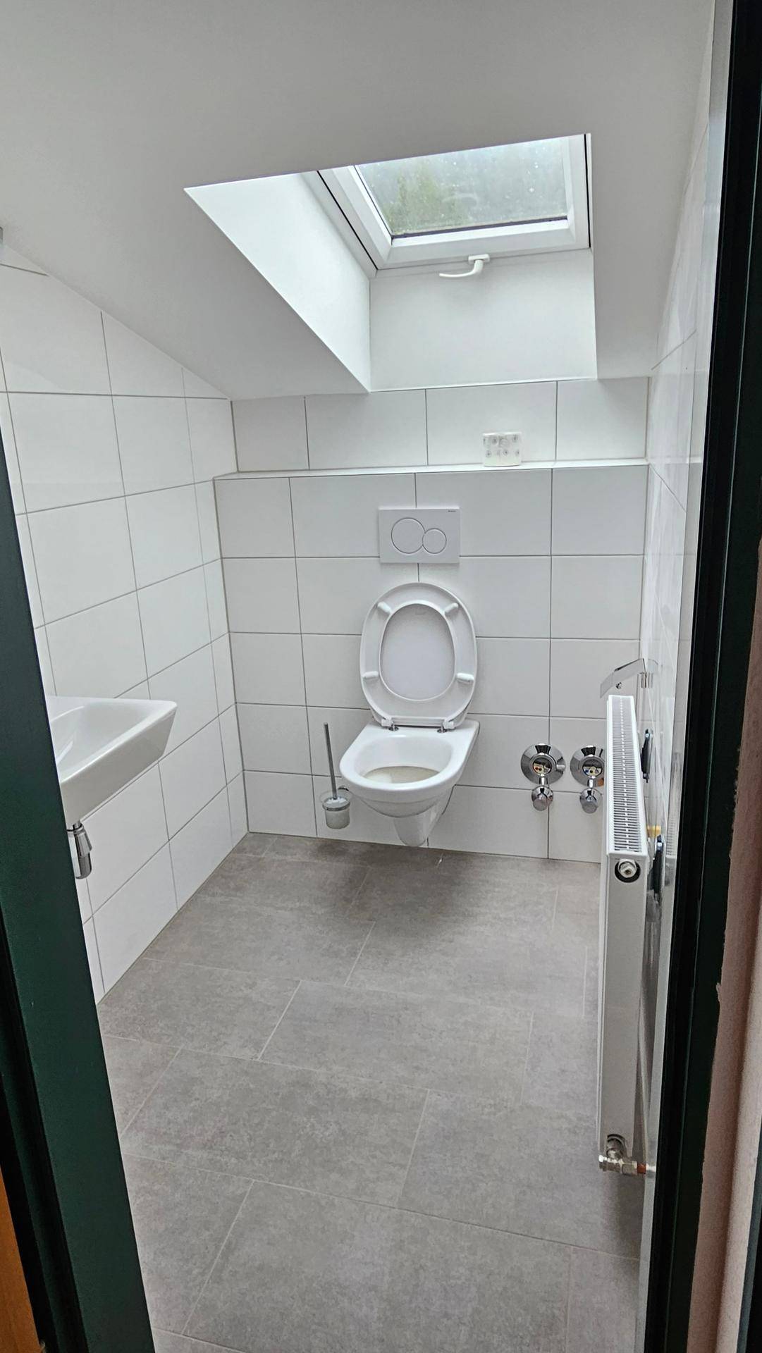 Modernes WC mit wandhängender Toilette, Waschbecken, Dachfenster und weißen Fliesen.