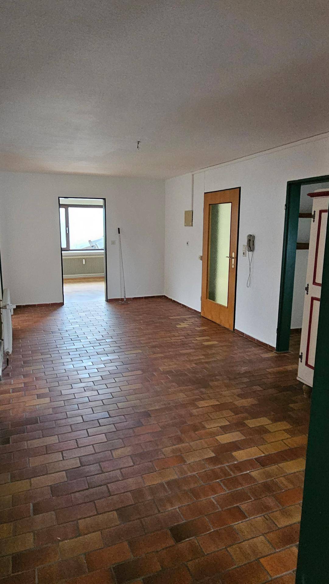 Großer Raum mit Terrakotta-Fliesenboden, weißen Wänden und Zugang zu weiteren Räumen.