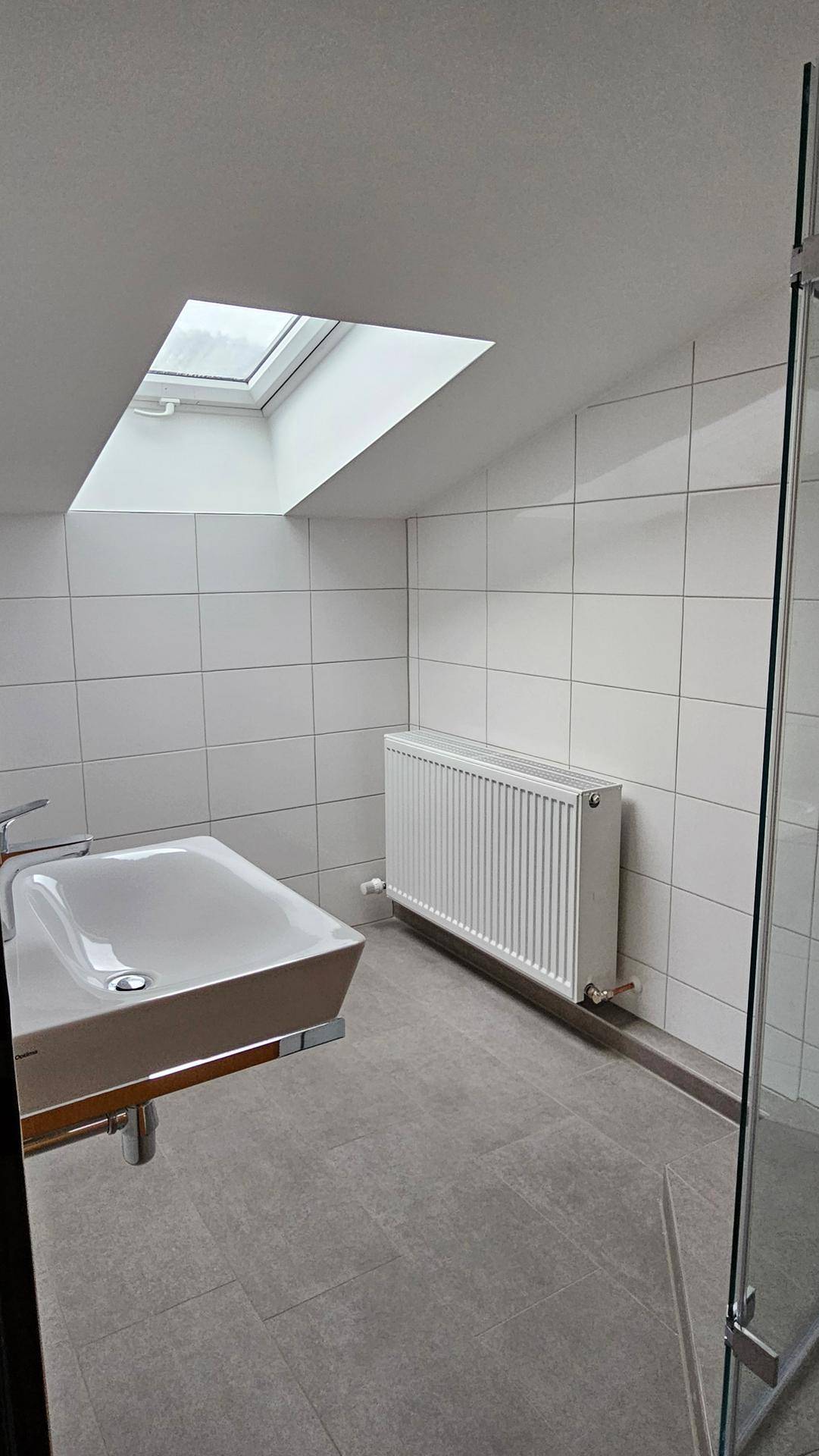 Modernes Badezimmer mit weißen Wandfliesen, grauem Boden und einem Dachfenster.