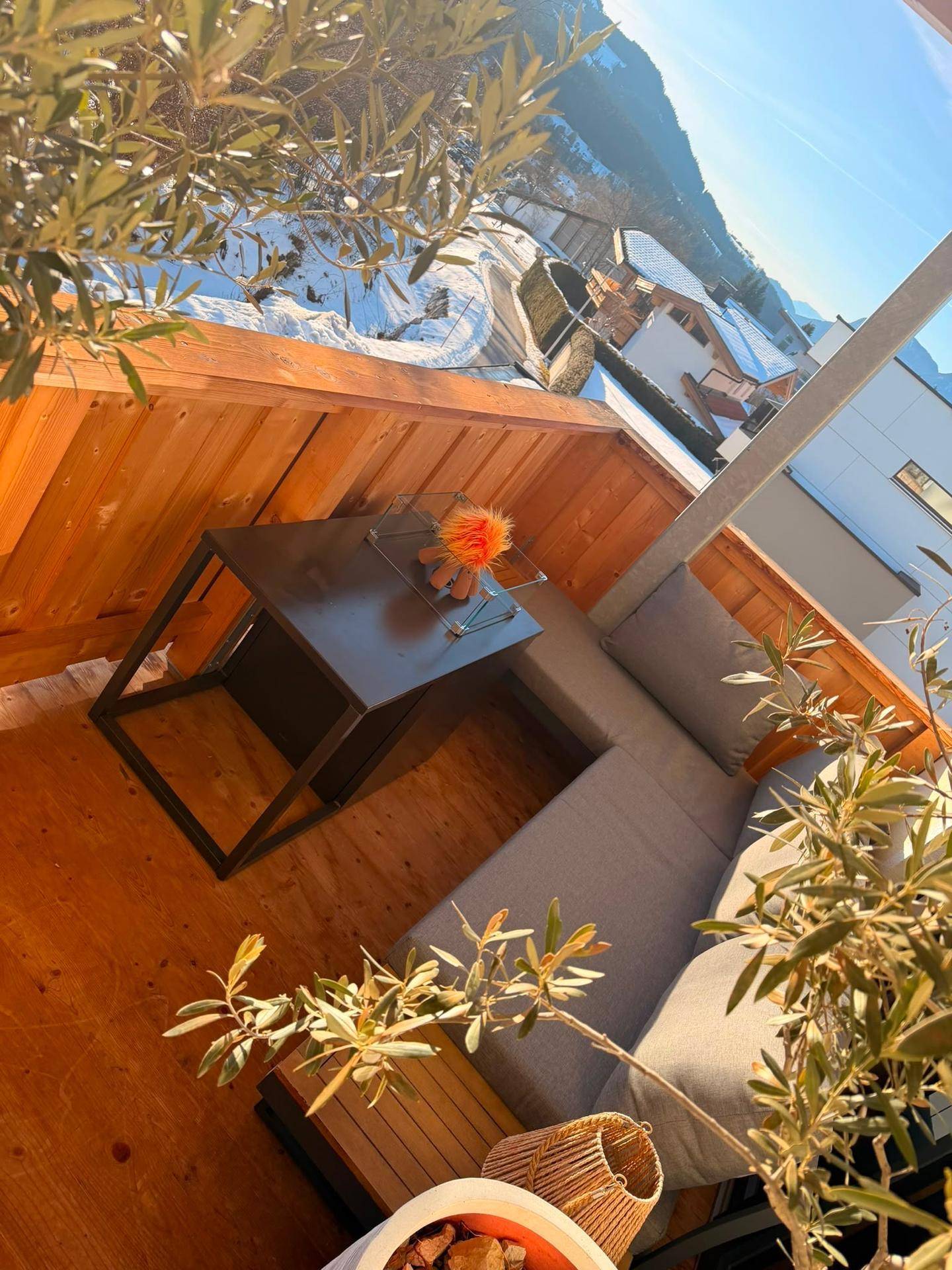 Sonniger Balkon mit Holzboden, bequemen Sitzmöbeln und Bergblick.