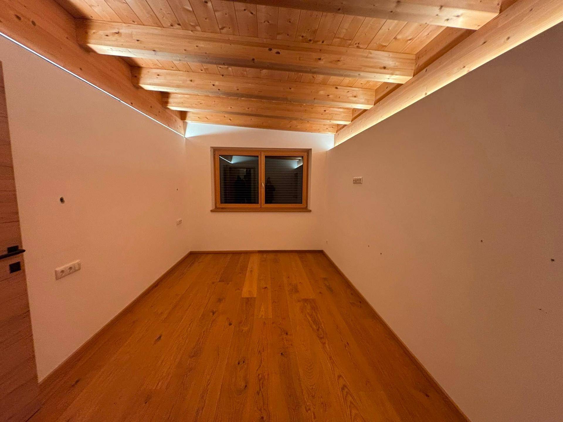 Gemütlicher Raum im Dachgeschoss mit Holzbalkendecke und Parkettboden.