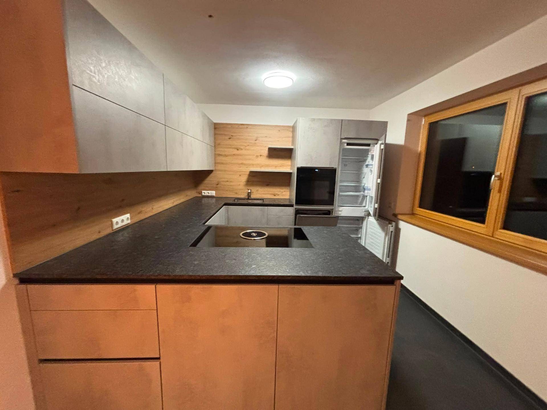 Moderne Einbauküche mit dunkler Arbeitsplatte, Holzdetails und integrierten Geräten.