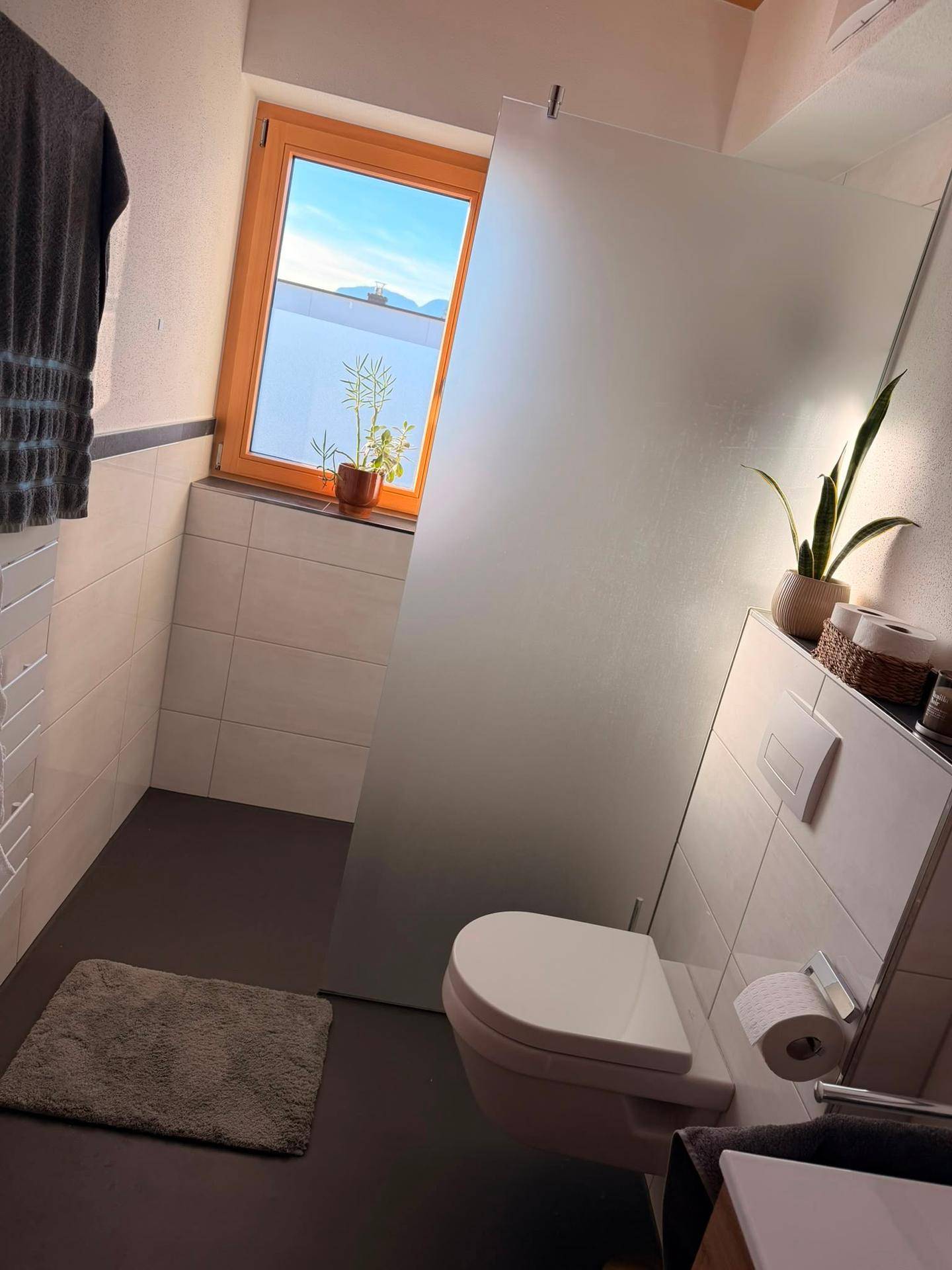 Modernes Badezimmer mit Dusche, wandhängendem WC und Fenster für Tageslicht.