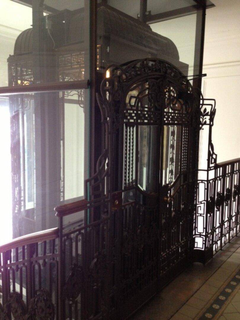 Historischer Aufzug mit kunstvollen Metallarbeiten und Glaswänden, der den Charme des alten Gebäudes unterstreicht.