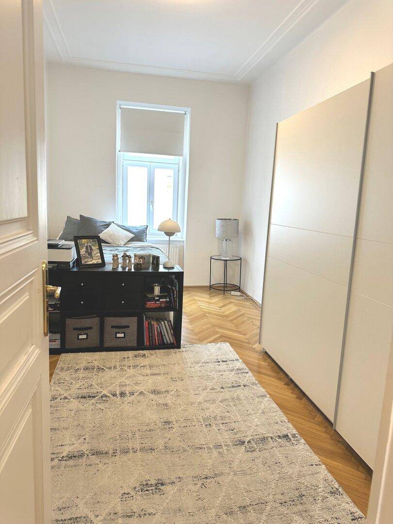 Schlafzimmer mit Fischgrätparkett, großem Kleiderschrank und einem Fenster.