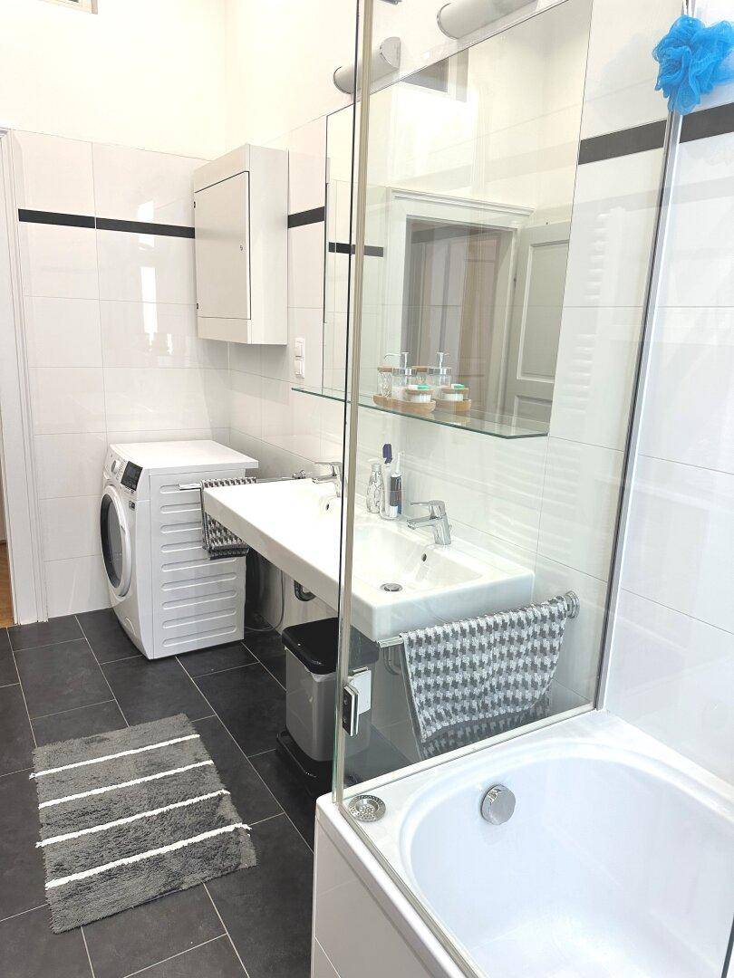 Helles Badezimmer mit Badewanne, Glasduschwand und Doppelwaschbecken.