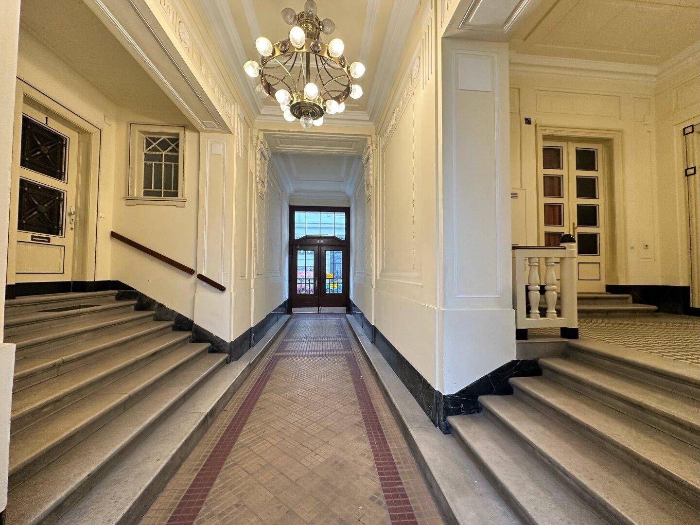 Repräsentativer Eingangsbereich mit breiter Treppe, Kronleuchter und klassischer Architektur.