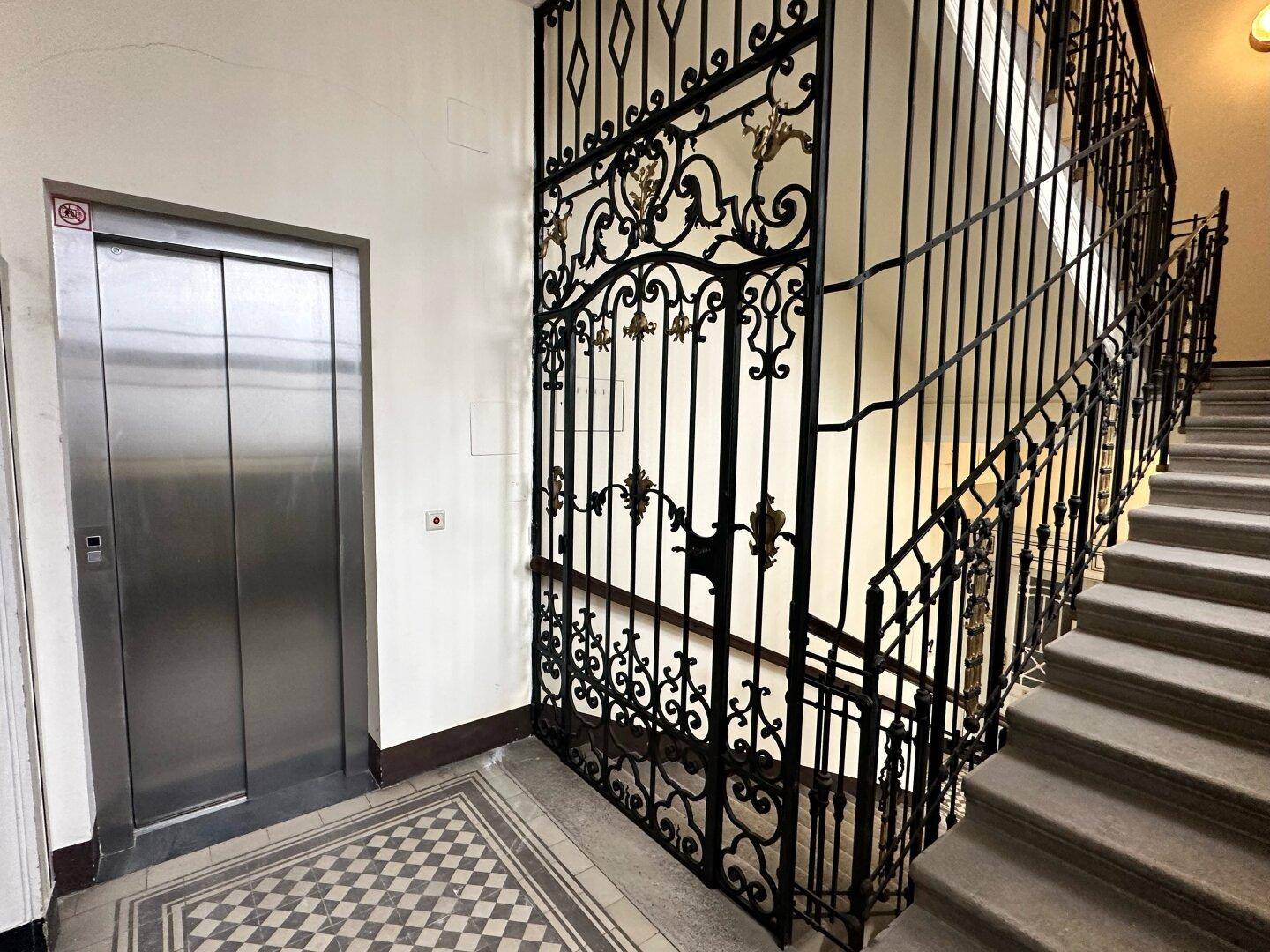 Historischer Hausflur mit elegantem Aufzug und kunstvollem schmiedeeisernem Treppengeländer.