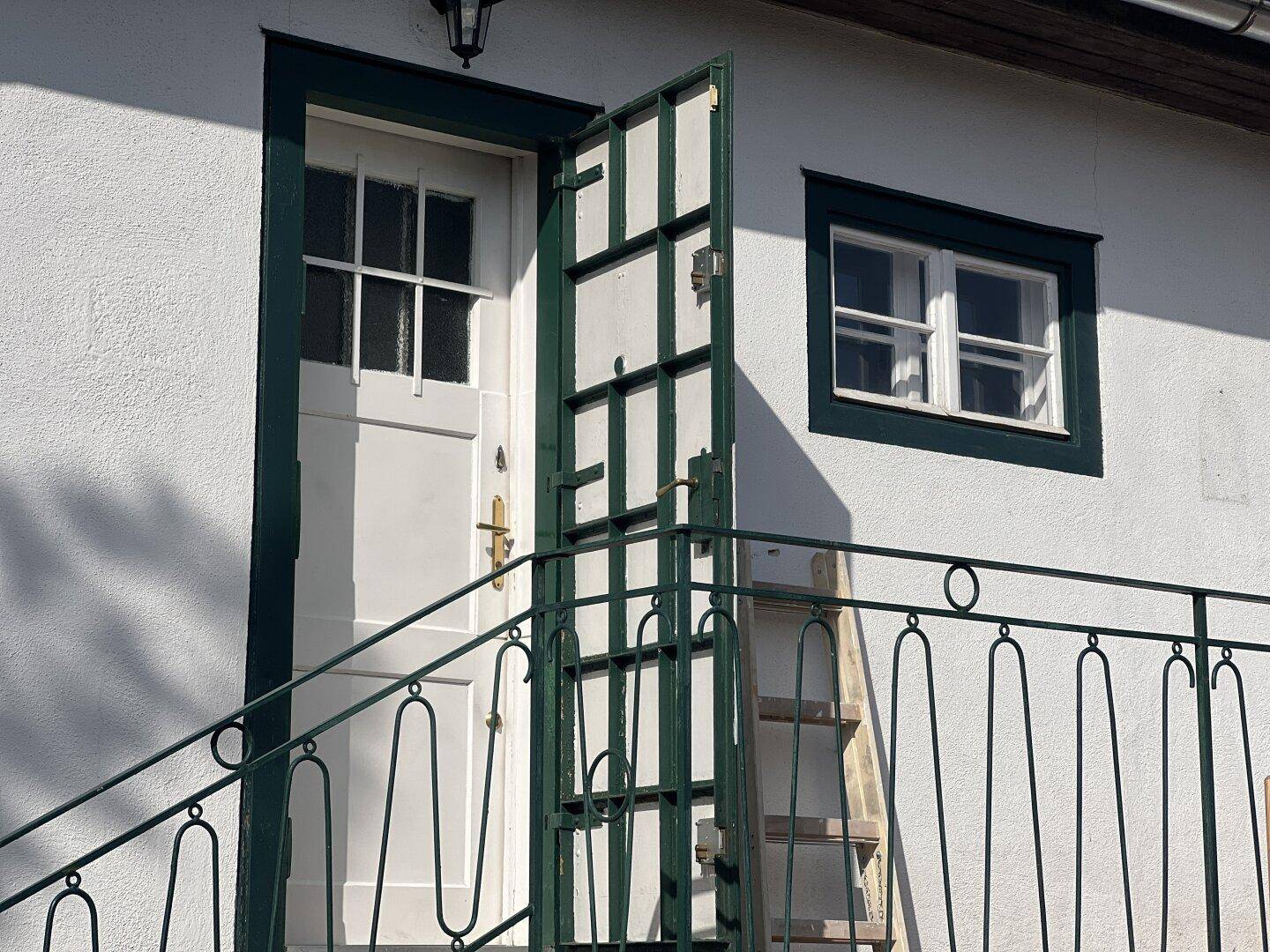 Traditioneller Hauseingang mit weißer Tür, grünem Rahmen und schmiedeeisernem Geländer.