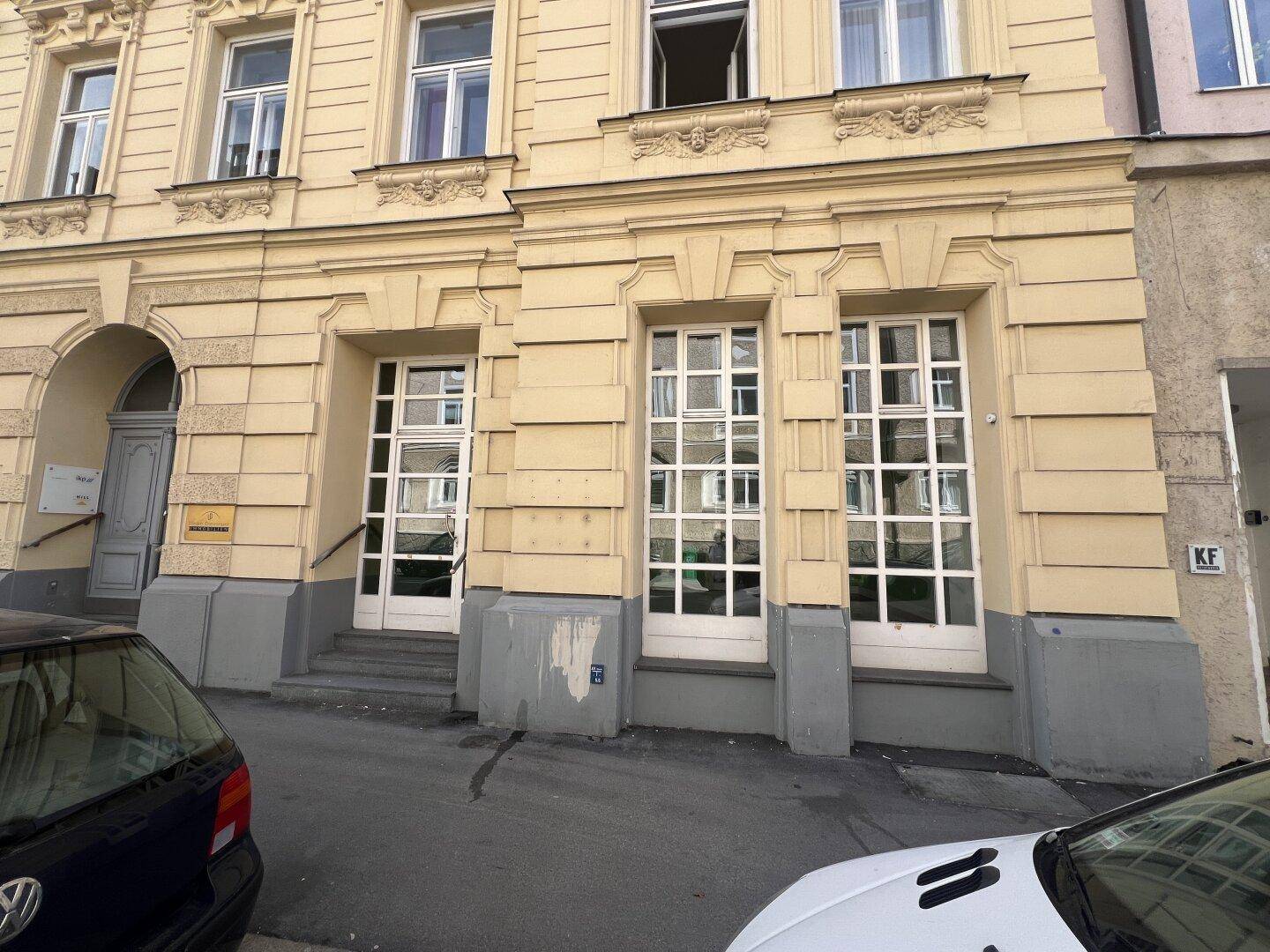 Historische Fassade eines Gebäudes mit großen Fenstern und Eingangstüren auf Straßenniveau.