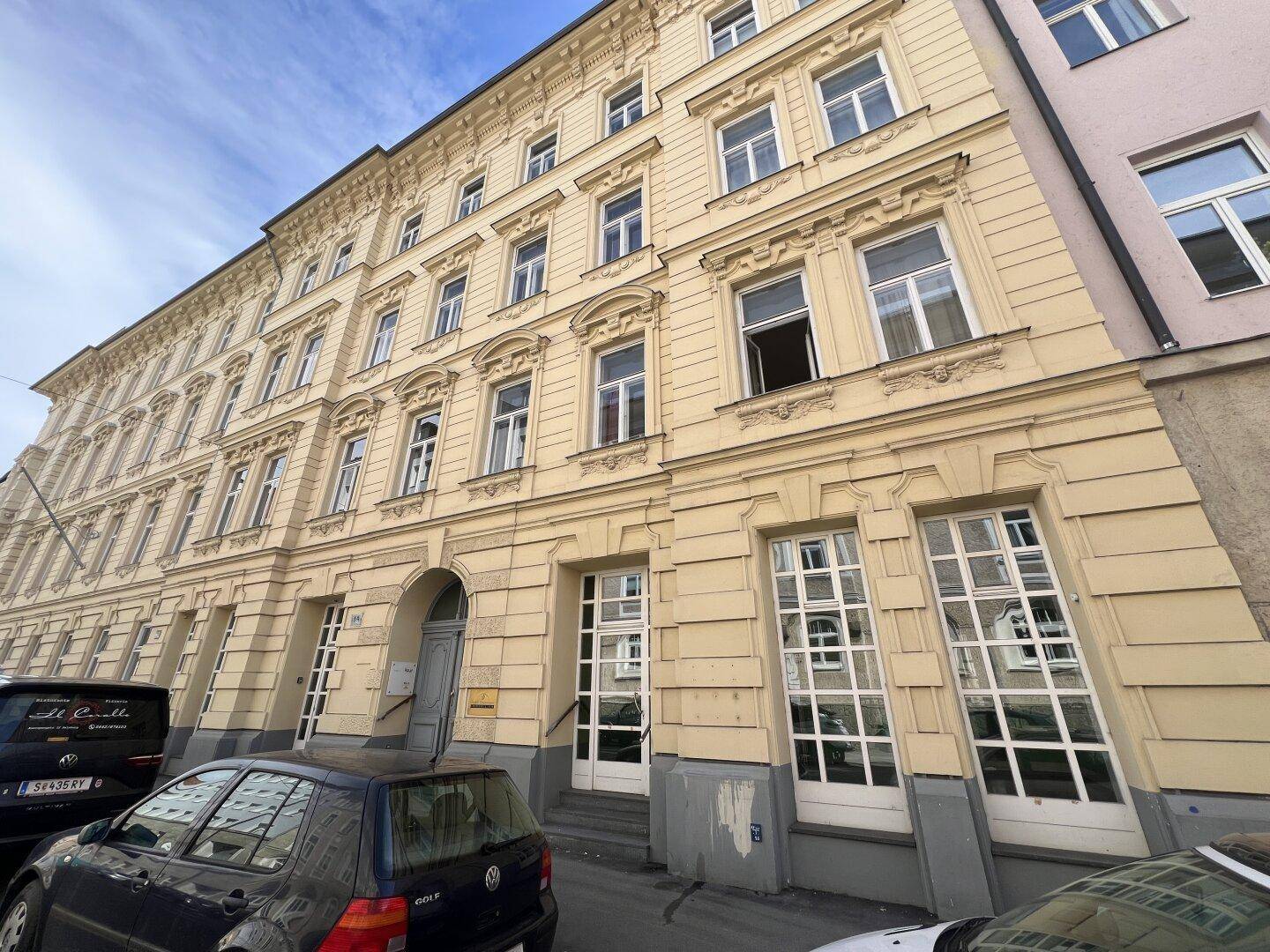 Ansicht eines mehrstöckigen Altbaus mit klassischer Fassade und vielen Fenstern an einer Straße.