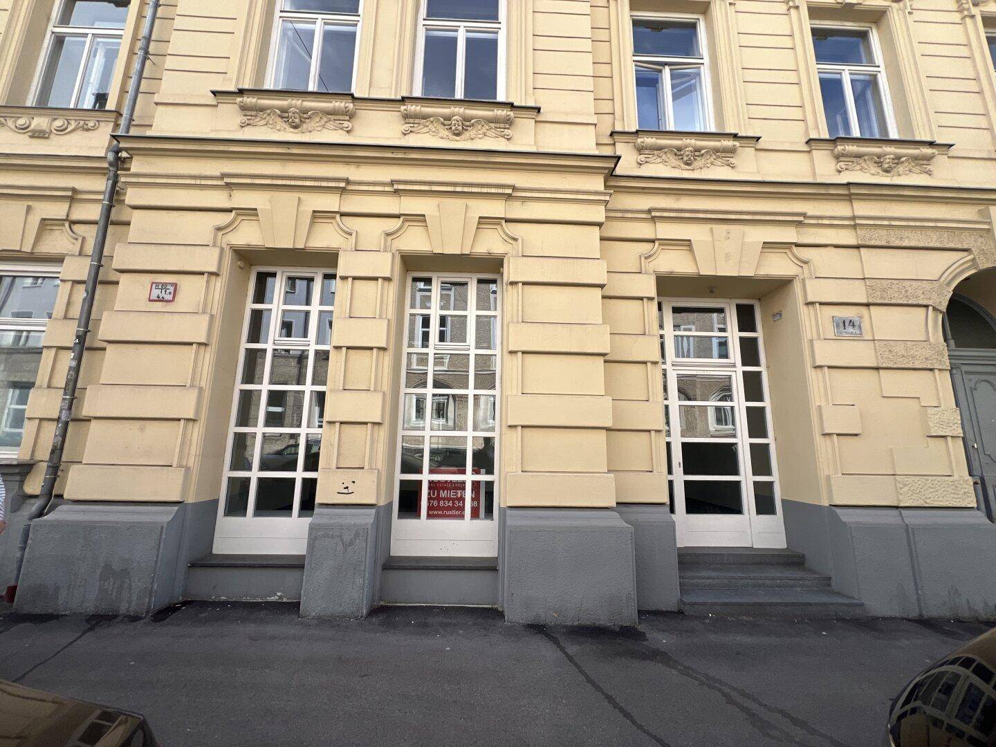 Historische Fassade eines Gebäudes mit hohen Fenstern und Eingangstüren zur Straße.
