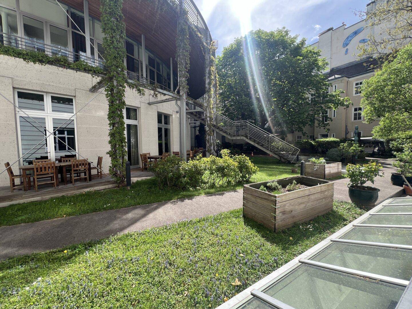 Grüner Innenhof mit Sitzgelegenheiten und üppiger Bepflanzung, umgeben von Gebäuden.