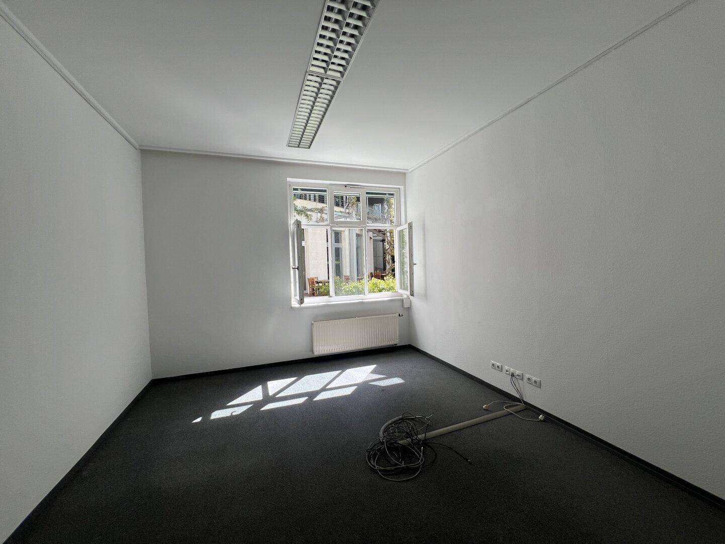 Leeres Büro mit Teppichboden und einem Fenster, das viel Tageslicht hereinlässt.