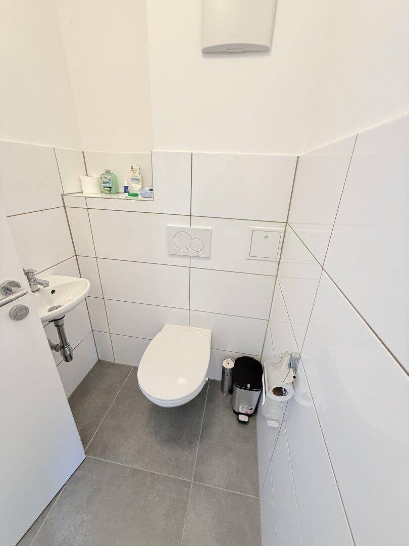 Kleines Gäste-WC mit Wand-WC, Waschbecken und modernen Fliesen.