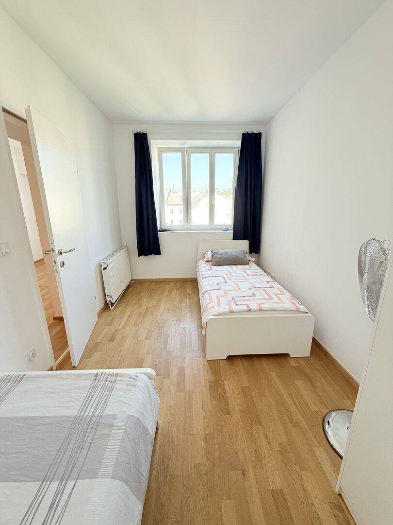 Helles Schlafzimmer mit zwei Einzelbetten, Parkettboden und Fenster, ideal für Kinder oder Gäste.