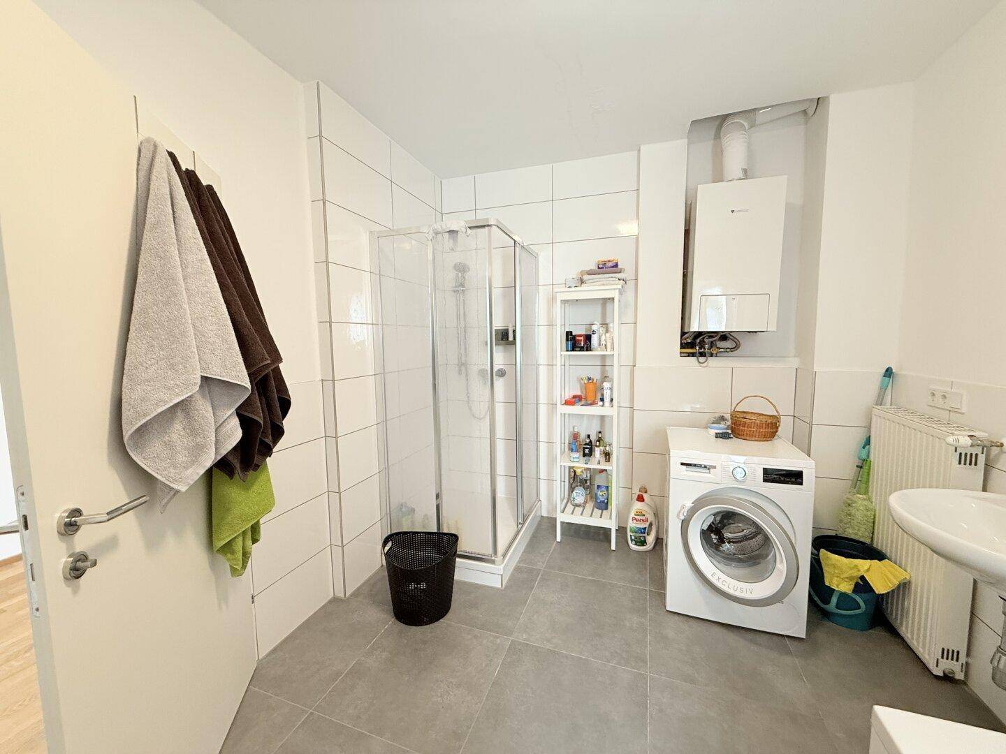 Funktionales Badezimmer mit Duschkabine, Waschbecken und Waschmaschine, hell gefliest.