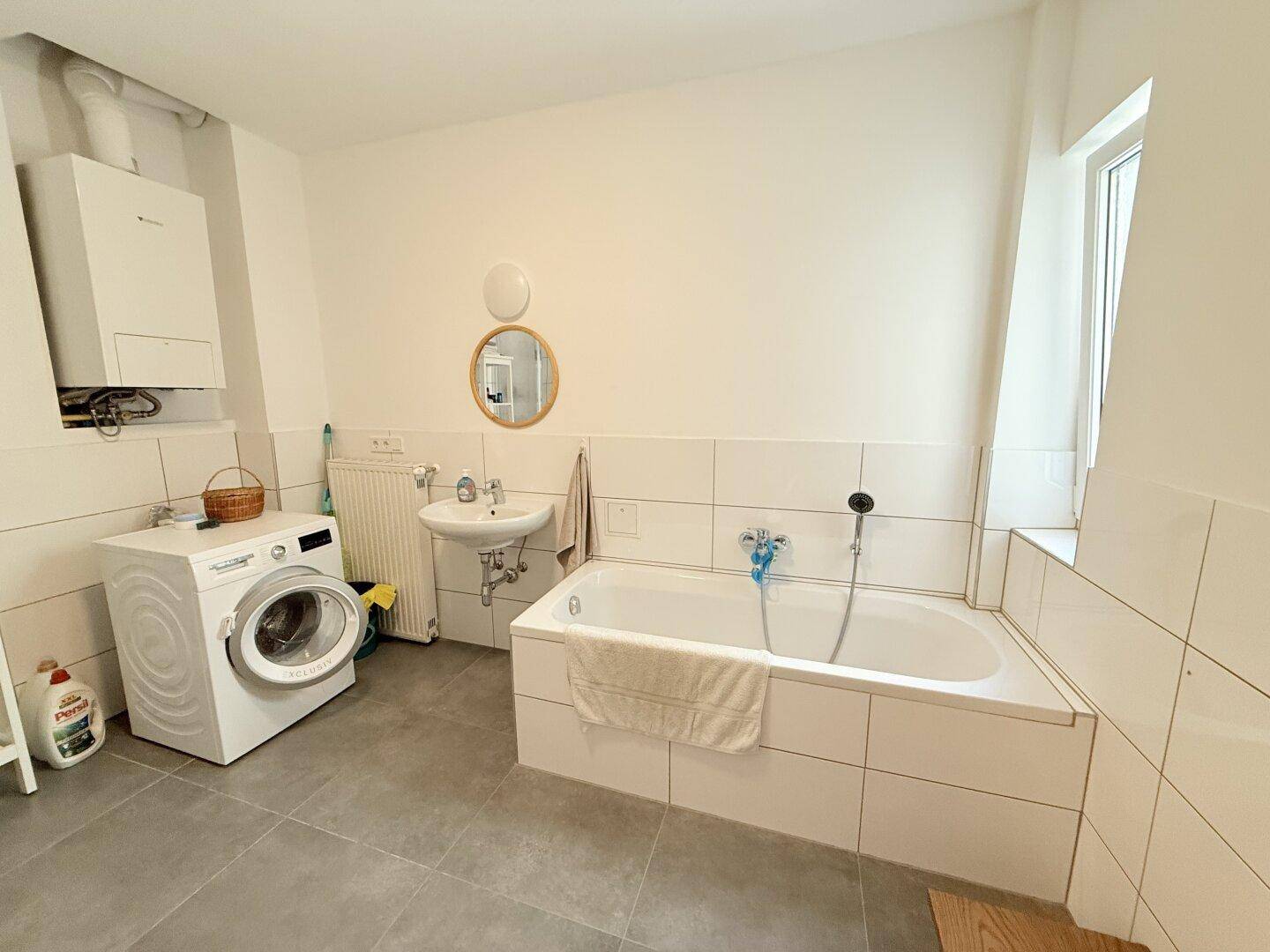 Geräumiges Badezimmer mit Badewanne, Waschbecken und Waschmaschine, hell und funktional.