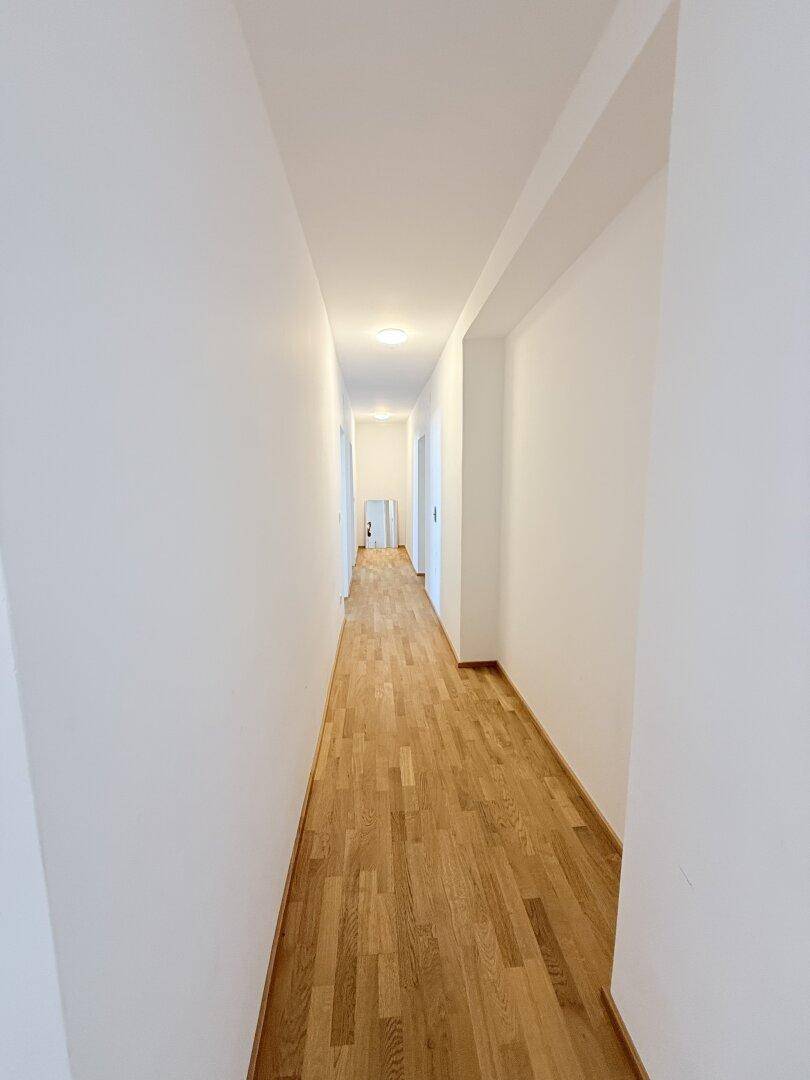 Langer, leerer Flur mit hellem Parkettboden und weißen Wänden, bietet viel Platz.
