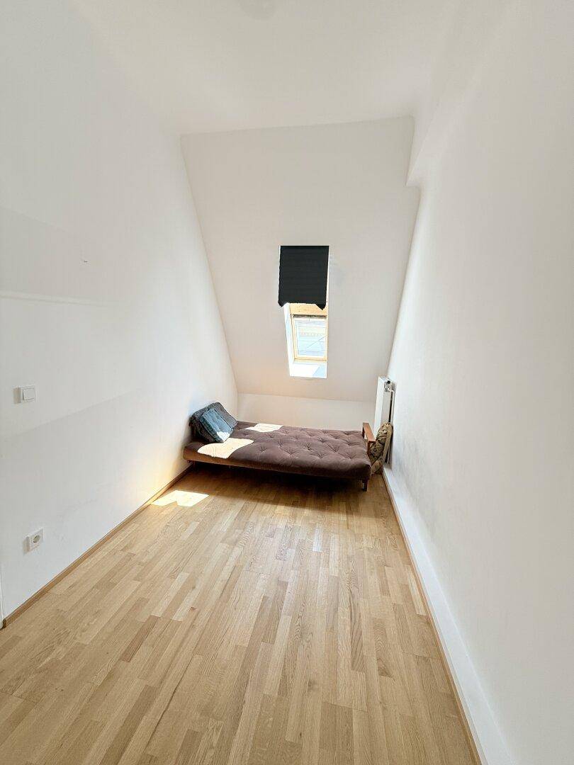 Gemütliches Zimmer mit Dachschräge, Parkettboden, Dachfenster und Futonbett.
