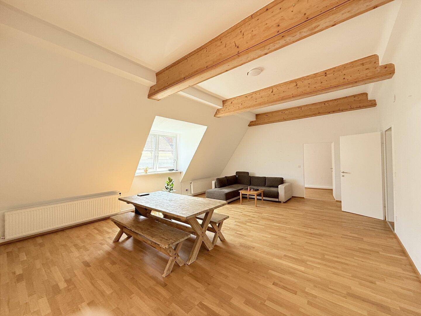Gemütlicher Wohn-Essbereich mit Holzbalken, Parkettboden und rustikalem Esstisch.