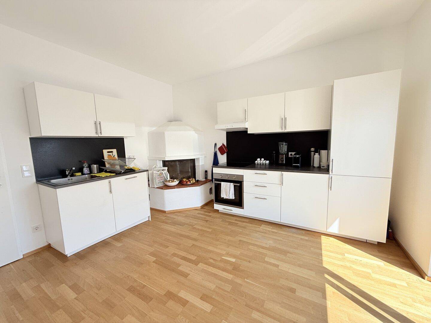 Moderne Einbauküche mit weißen Schränken, dunkler Arbeitsplatte und integriertem Kamin.