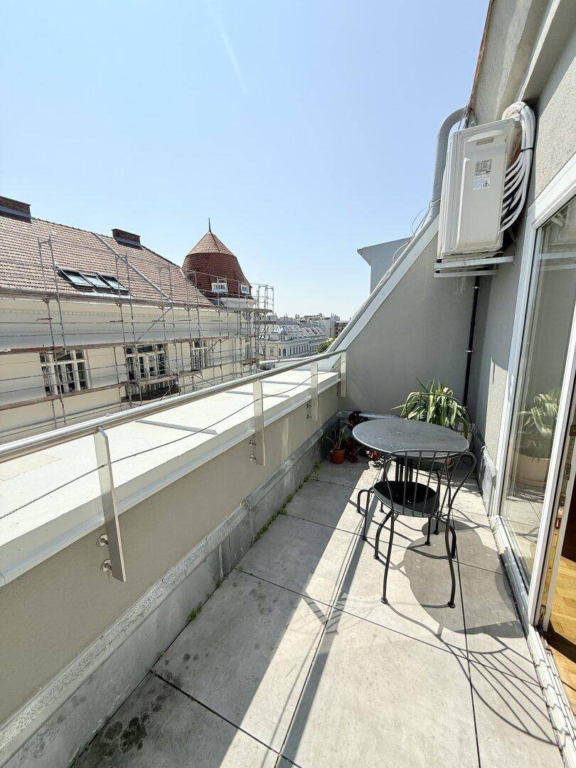 Schmaler Balkon mit Stadtblick, Sitzgelegenheit und Klimaanlage-Außengerät.