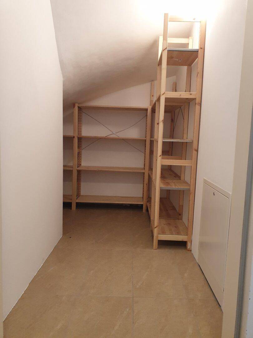 Praktischer Abstellraum mit Holzregalen und schrägen Wänden, bietet viel Stauraum.