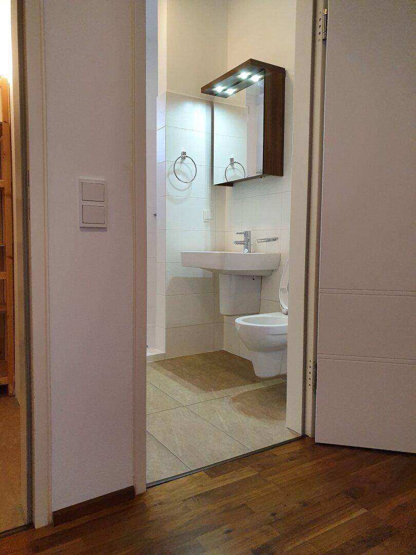 Kleines, modernes WC mit wandhängender Toilette und Waschbecken, hell gefliest.
