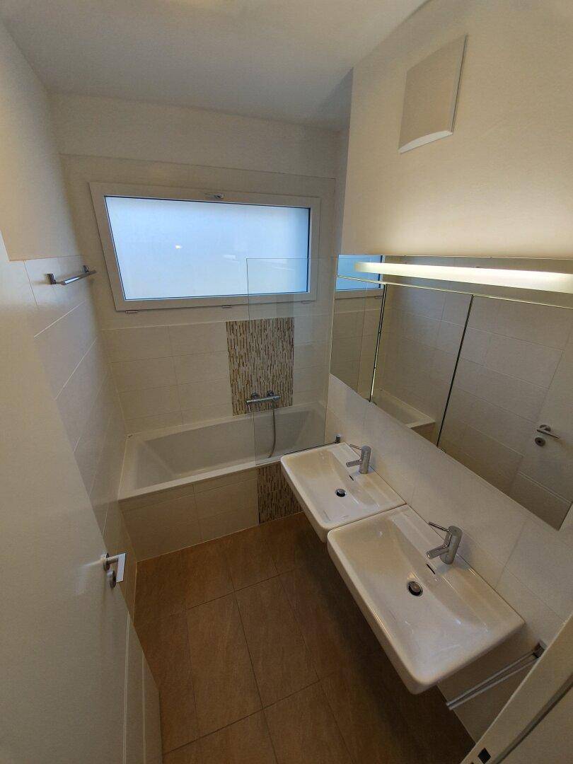 Helles Badezimmer mit Badewanne und zwei Waschbecken, ausgestattet mit einem Spiegelschrank.