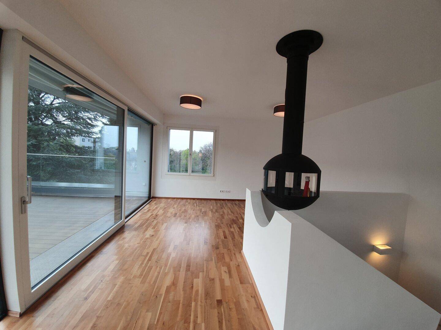 Heller Wohnbereich mit Holzboden und stilvollem Hängekamin, große Fensterfronten zur Terrasse.