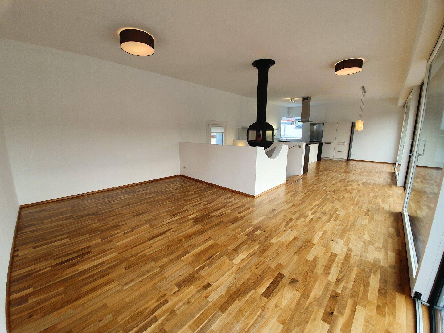 Geräumiger Wohnbereich mit Holzboden und modernem Hängekamin, offen zur Küche gestaltet.