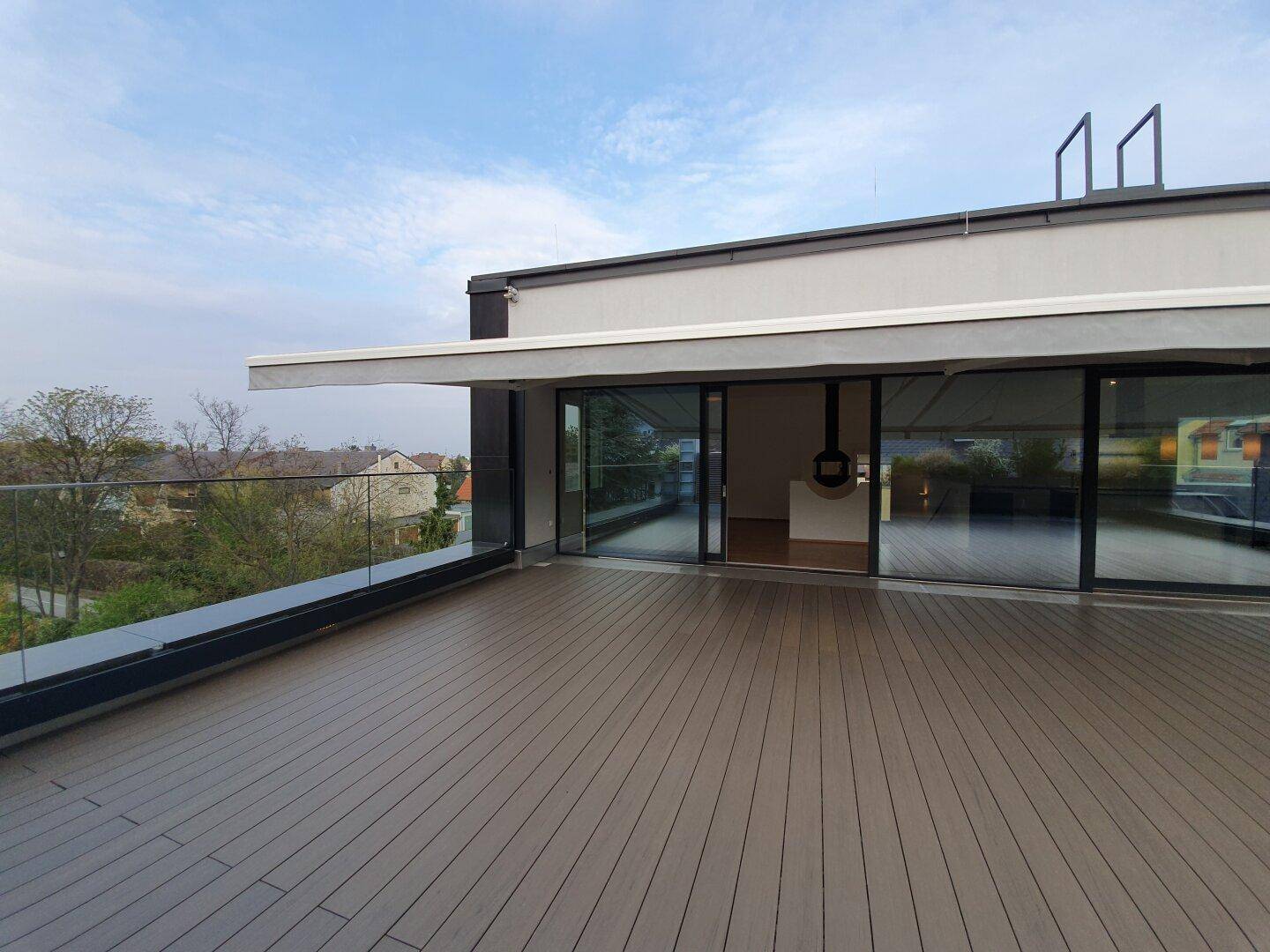 Weitläufige Terrasse mit Glasgeländer und ausgefahrener Markise, bietet einen schönen Ausblick.