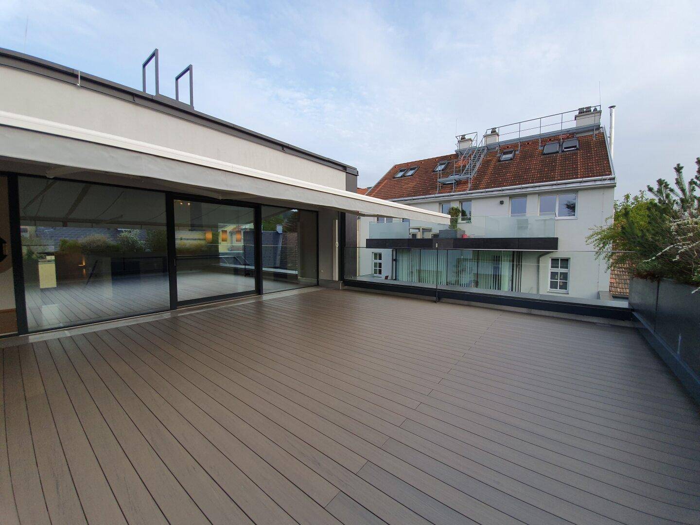 Geräumige Dachterrasse mit Holzboden und Blick auf die umliegenden Gebäude und Dächer.