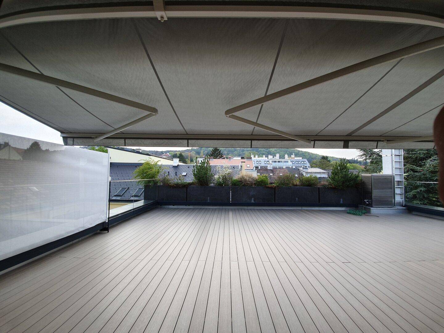 Geräumige Terrasse mit Holzdeck, ausfahrbarer Markise und Blick auf die Umgebung.