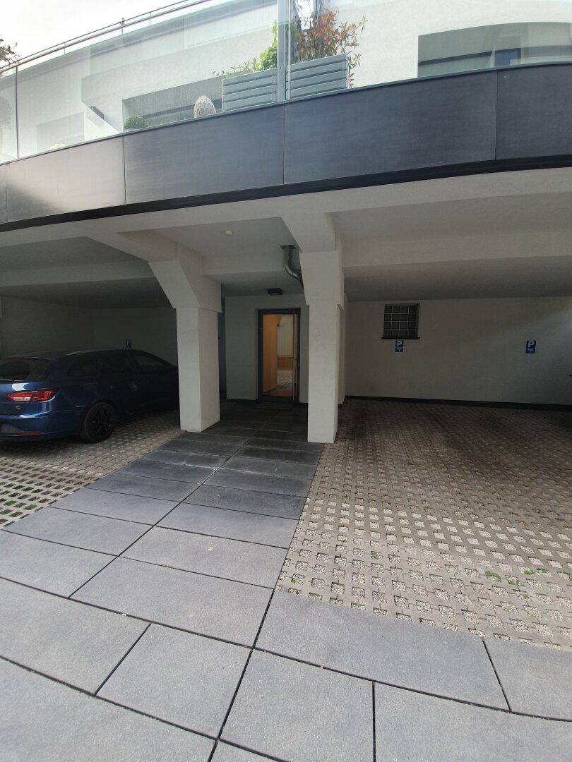 Überdachter Parkbereich mit einem Auto und Zugang zu einem Gebäude.