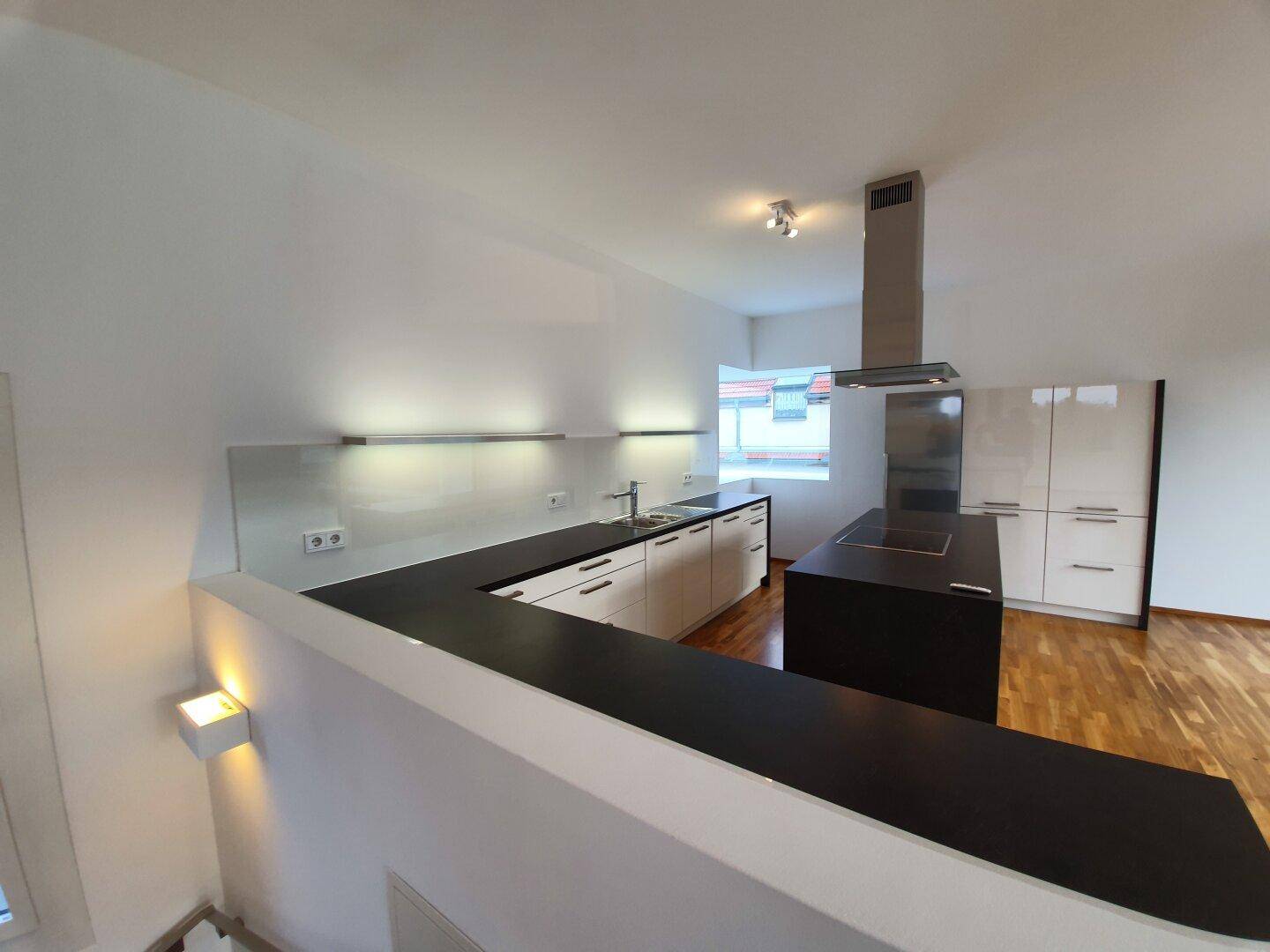 Moderne Einbauküche mit weißen Schränken und dunklen Arbeitsplatten, integriert in den offenen Wohnraum.