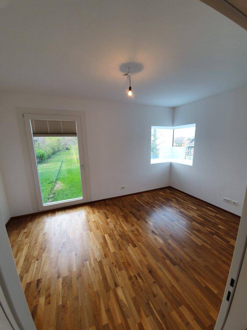 Helles Schlafzimmer mit Holzboden und großen Fenstern, bietet einen Blick ins Grüne.