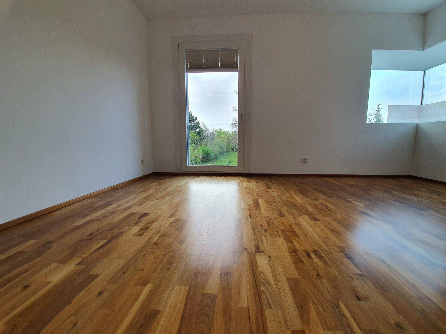 Geräumiges Schlafzimmer mit Holzboden und großen Fenstern, bietet viel Tageslicht.