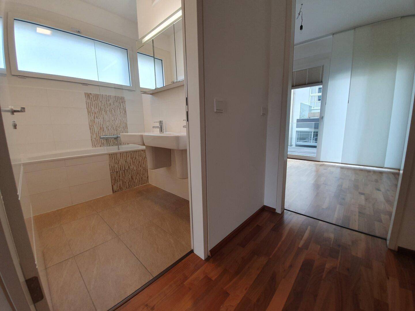 Modernes Badezimmer mit Badewanne und Doppelwaschbecken, angrenzend an einen weiteren Raum.
