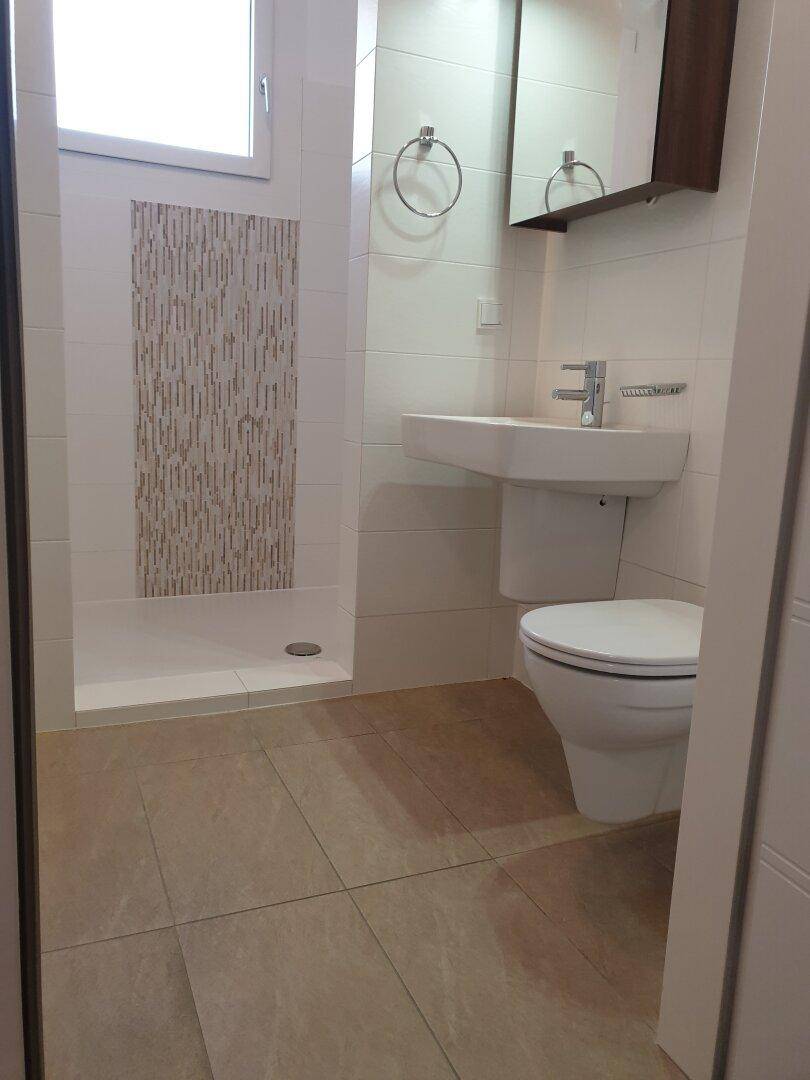 Modernes Badezimmer mit ebenerdiger Dusche und wandhängender Toilette, hell gefliest.