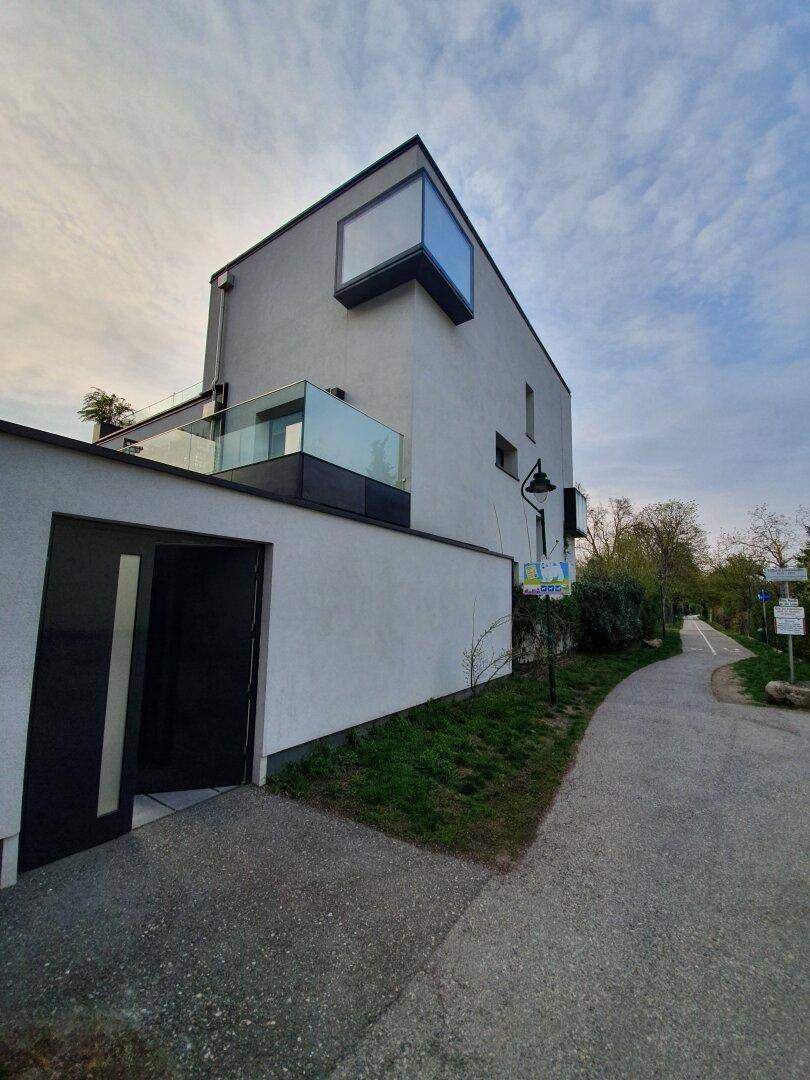 Moderne Architektur mit weißer Fassade, großen Fenstern und einem Glasbalkon.