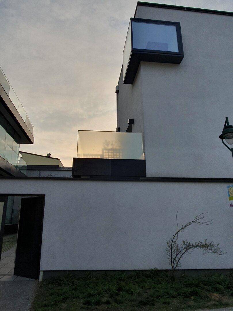 Detailansicht der modernen Fassade mit Glasbalkon und markantem Eckfenster.