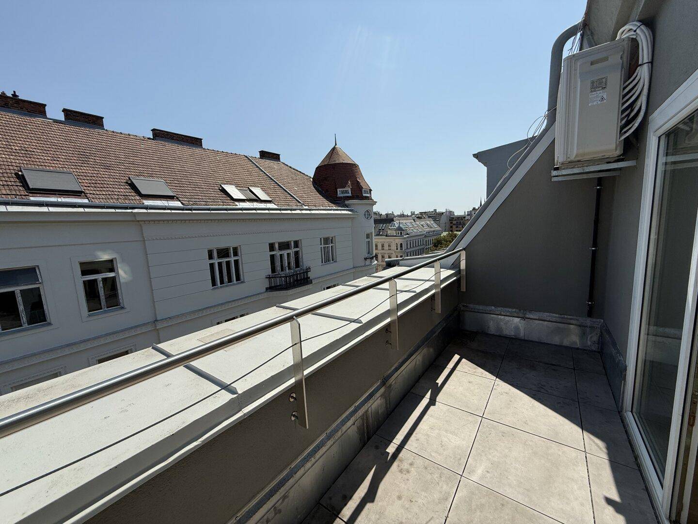 Langer Balkon mit Blick über die Dächer der Stadt und moderner Brüstung.