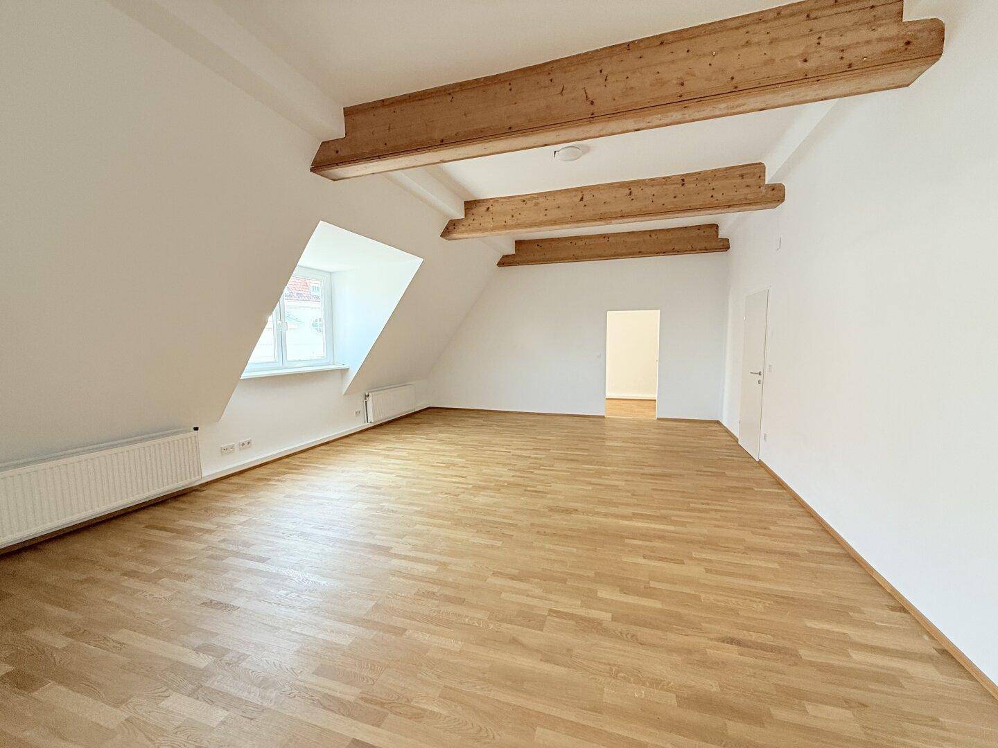 Heller Raum mit Holzbalken, Dachschräge und Parkettboden, bietet vielseitige Nutzungsmöglichkeiten.