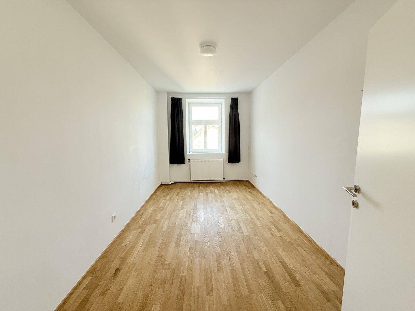 Helles Schlafzimmer mit Parkettboden und Fenster, bereit zur individuellen Einrichtung.