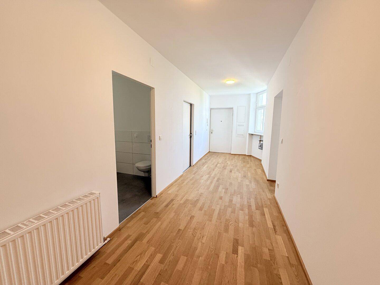 Heller Flur mit Parkettboden und Zugang zu einem Badezimmer oder Gäste-WC.