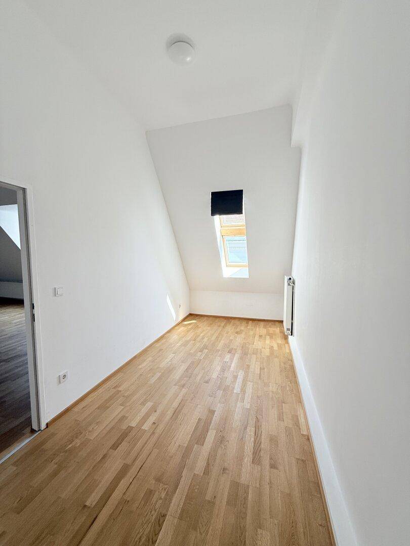 Helles Zimmer mit Dachschräge, Parkettboden und Dachfenster, ideal als Schlaf- oder Arbeitszimmer.